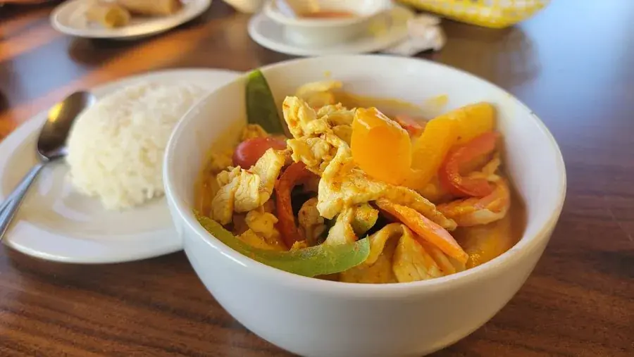 Chicken Thai curry with bell peppers in a bowl beside jasmine rice at Polly's Thai Food in Lawton, OK